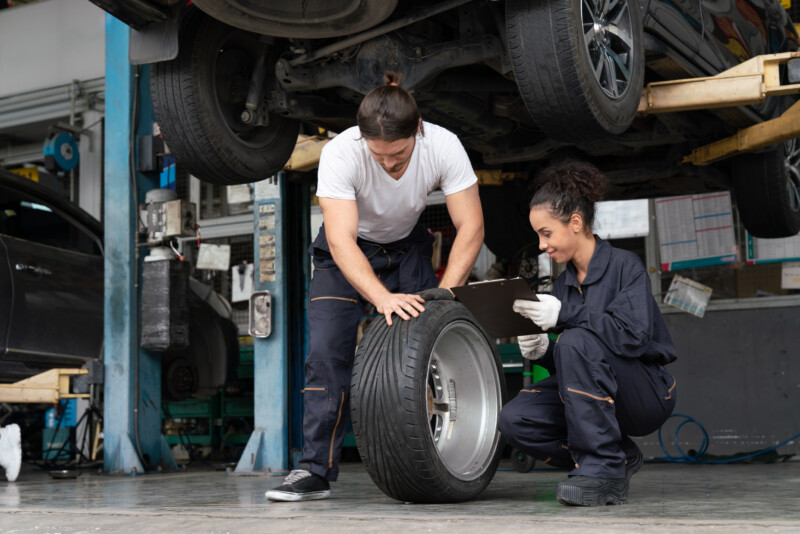 Mechanics man and woman checking and repairing tire wheel a car in garage. Group technician in uniform repair and maintenance of car at auto car service shop.