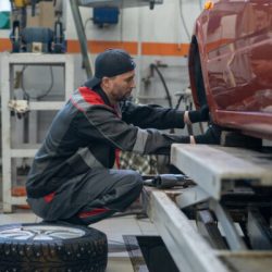 Side view full length portrait of male mechanic changing tires on car while working in auto repair shop